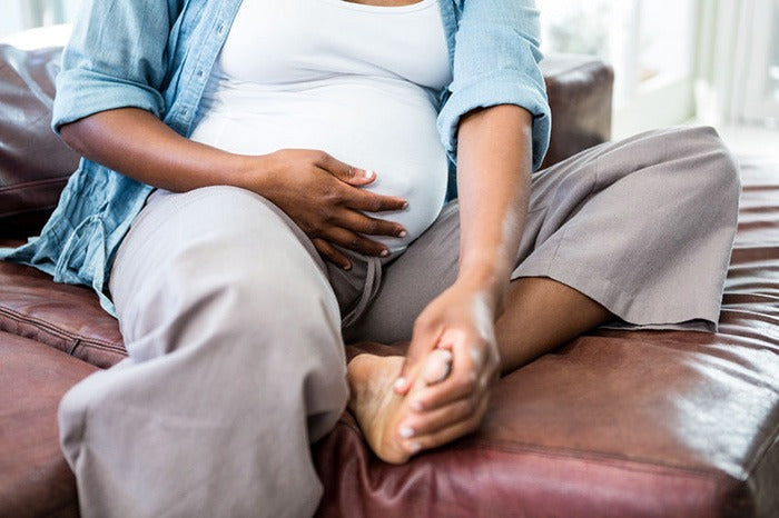 barefoot and clothed pregnant woman gripping her belly and left foot