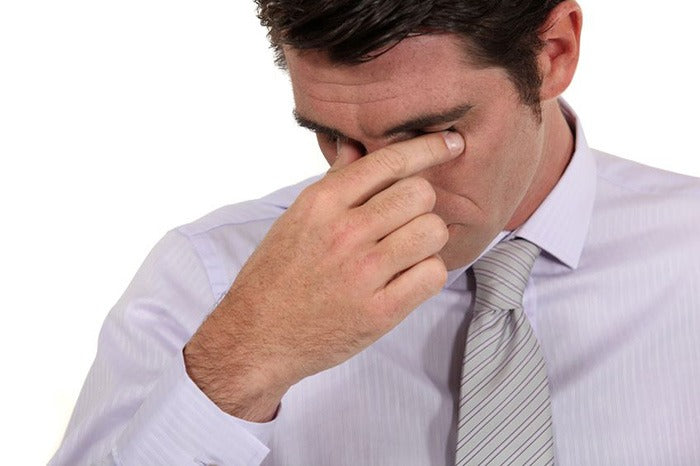 man in tie pressing fingers to his closed eyes in pain