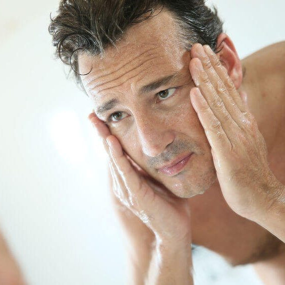 man gripping his face while observing intently in the mirror